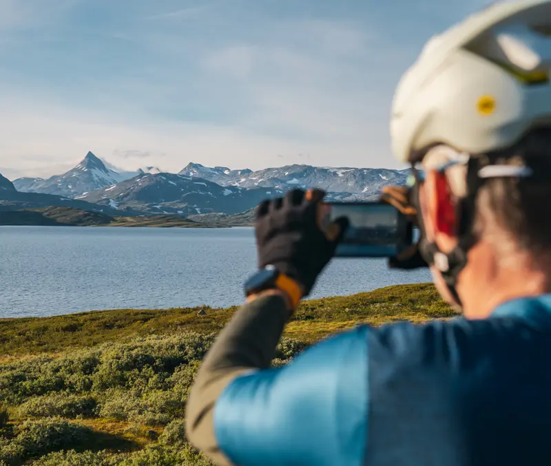 Mann med sykkel tar bilde av fjelltoppen Uranostind ved Tyinvatnet