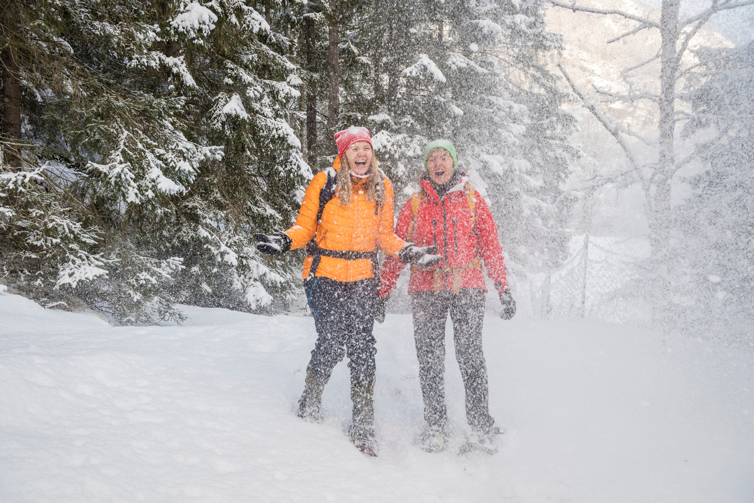 To kvinner på truger som smiler og ler og kaster snø i luften