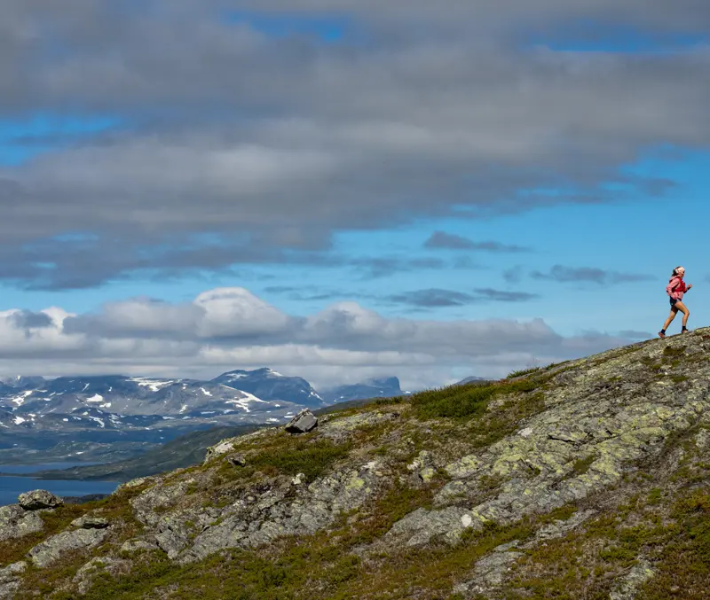 Trailrunner i høyfjellet – ung kvinne løper med Jotunheimen sine majestetiske fjell i bakgrunnen