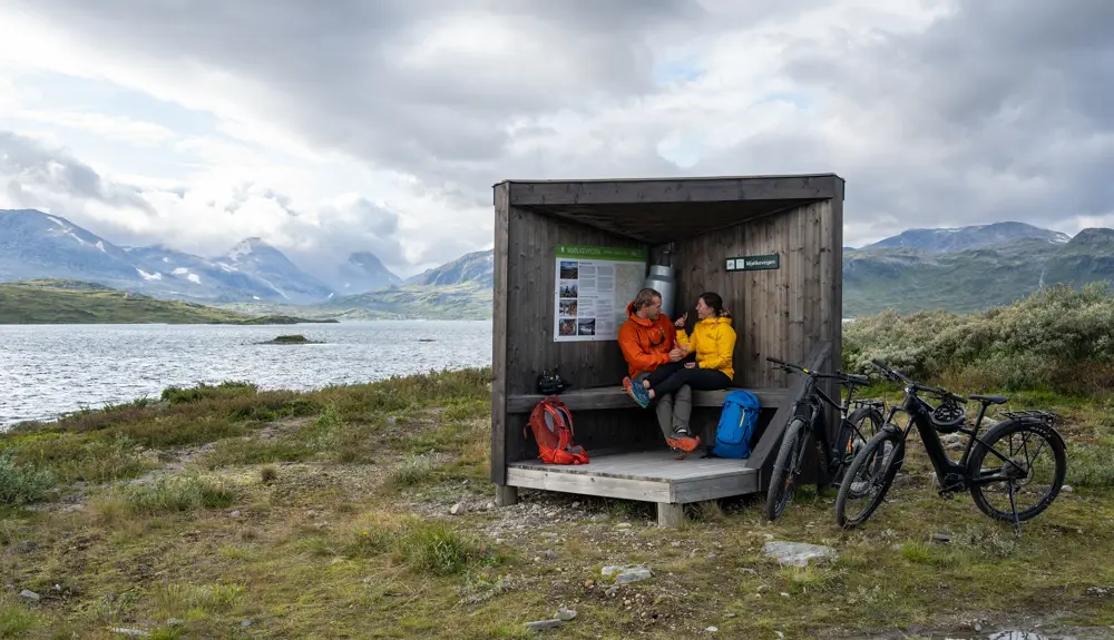Ungt par på sykkeltur på Mjølkevegen langs Tyin tar matpause ved et informasjonspunkt